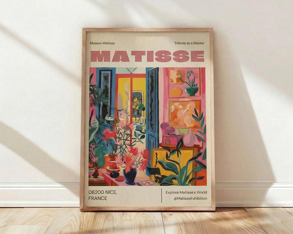 May include: Framed vintage-style poster featuring Henri Matisse's colorful interior scene with tropical plants, open blue shutters, and vibrant artwork on walls in pink, yellow, orange and green tones. Text reads "MATISSE" and "06200 NICE, FRANCE" on cream background. Natural wood frame sits on light wooden floor against white wall with soft shadows.