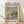 May include: Framed art print of Monet's impressionist painting showing sailboats with white sails on blue water, with green trees and buildings along the shoreline. The poster features "CLAUDE MONET EXHIBITION GALLERY" text at top and "Regattas at Argenteuil 1872" at bottom on cream background. Light wood frame sits against white wall on blonde hardwood floor with natural sunlight shadows.