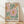 May include: Framed botanical poster print with colorful stylized flowers in pink, orange, and yellow with green foliage on cream background, featuring "NO RAIN, NO FLOWERS" text at bottom. Natural wood frame leaning against white wall on light wooden floor with soft sunlight shadows.