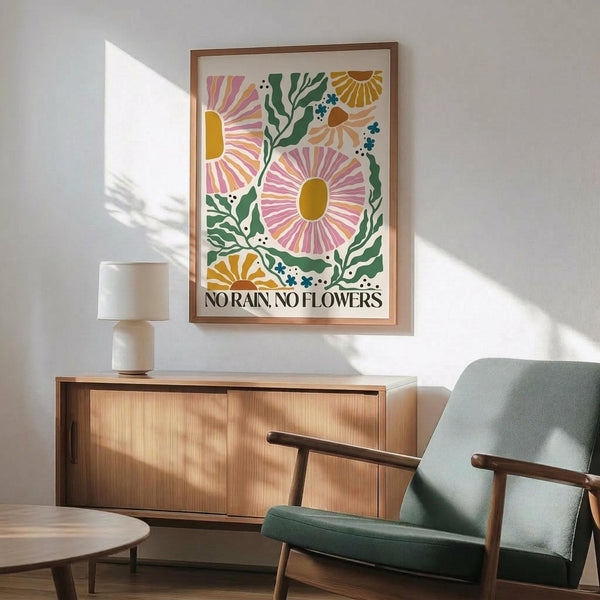 May include: Colorful botanical poster with stylized flowers in pink, yellow, and orange with green foliage, featuring "No Rain, No Flowers" text at bottom, displayed in thin wooden frame above mid-century modern credenza with ceramic lamp, next to sage green upholstered armchair in bright sunlit room with white walls