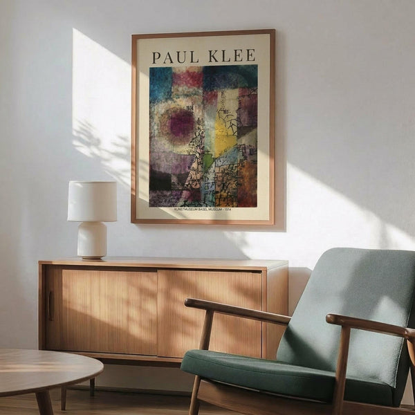 May include: Paul Klee abstract art print in wooden frame hanging above mid-century modern wooden credenza with white table lamp. Mint green upholstered armchair with wooden frame sits nearby. Poster features colorful geometric and organic shapes in blues, reds, yellows, and earth tones with intricate line work. Warm natural lighting creates shadows across white wall in minimalist living room setting.
