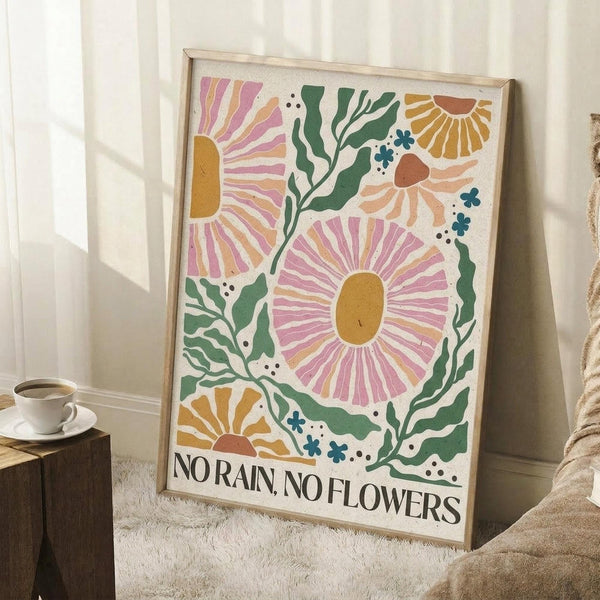 May include: Framed botanical poster with colorful illustrated flowers in pink, orange, and yellow with green leaves scattered across cream background, text reading "NO RAIN, NO FLOWERS" at bottom in black letters. Light wood frame leaning against white wall corner next to small wooden side table with white coffee cup and saucer, beige textured rug visible on floor.