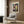 May include: Paul Klee abstract art poster with colorful geometric squares and circular forms in blues, reds, yellows and earth tones, displayed in light wood frame on textured wood wall above modern beige armchair with geometric patterned pillow, next to brass floor lamp and dark round side table with open book