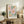May include: Framed botanical poster with colorful daisy-like flowers in pink, orange, and yellow with green foliage and "No Rain, No Flowers" text below, displayed on rustic wood sideboard next to fern plant, books, and ceramic vase in neutral-toned living room setting