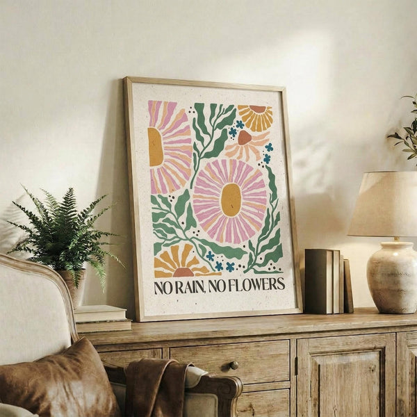 May include: Framed botanical poster with colorful daisy-like flowers in pink, orange, and yellow with green foliage and "No Rain, No Flowers" text below, displayed on rustic wood sideboard next to fern plant, books, and ceramic vase in neutral-toned living room setting