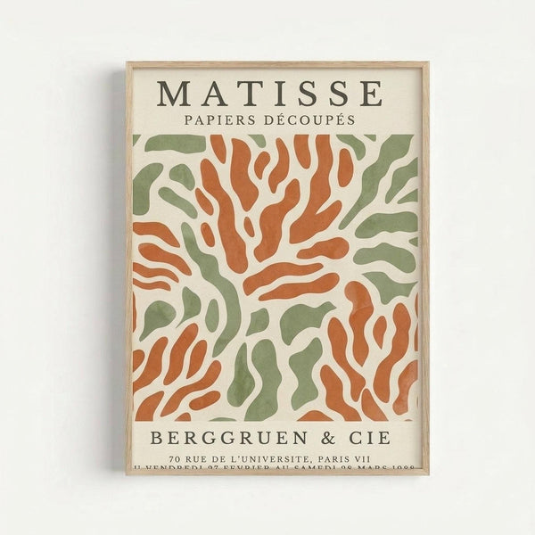 Framed vintage-style art poster featuring abstract organic shapes in terracotta orange and sage green on cream background. Text reads "MATISSE PAPIERS DÉCOUPÉS" at top and "BERGGRUEN & CIE" with Paris gallery address below the flowing, cut-paper inspired design. Light wood frame against white wall.