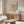 May include: Matisse exhibition poster with orange and green abstract coral-like cutout design, displayed above mid-century walnut credenza in minimalist living room with cream chair, glass coffee table, and brass floor lamp against white walls