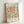 May include: Framed exhibition poster featuring Matisse's cut-out paper style artwork with flowing organic shapes in orange and sage green on cream background. Light wood frame displays the vintage 1988 Berggruen & Cie gallery poster, leaning against white wall with soft natural lighting casting gentle shadows.