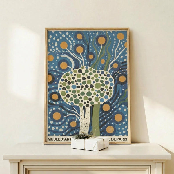 May include: Framed art print displaying stylized tree with circular dotted foliage in greens and blues against swirling blue background with orange orbs, sitting on light wood surface next to small wrapped gift with twine and greenery sprig against white wall