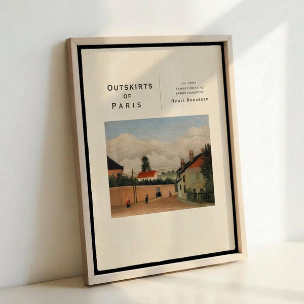 May include: Framed art print featuring Henri Rousseau's pastoral painting of a French village street scene with small figures walking along a dirt road between colorful houses under a cloudy blue sky. The cream-colored poster has black text reading "Outskirts of Paris" and artist information. Displayed in a thin light wood frame with black matting, leaning against a white wall.