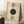 May include: Modern geometric art print in wooden frame leaning against white wall corner. Features abstract circles in sage green, beige, and cream with concentric line patterns and dotted details on textured paper background. Text reads "MODERN" and "BAUHAUS" vertically. Scene includes wooden side table with white coffee cup, beige throw blanket, and white textured rug in bright natural lighting.