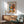 May include: Framed Matisse-style art poster hanging on white wall above wooden sideboard, featuring colorful still life with vase of flowers and oranges in blue and coral tones. Mid-century modern room setting with mint green upholstered chair, white table lamp, and natural sunlight shadows creating warm ambiance.