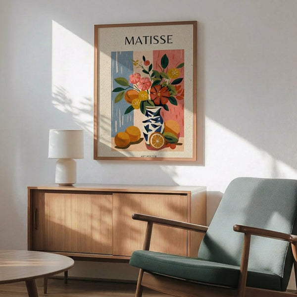 May include: Framed Matisse-style art poster hanging on white wall above wooden sideboard, featuring colorful still life with vase of flowers and oranges in blue and coral tones. Mid-century modern room setting with mint green upholstered chair, white table lamp, and natural sunlight shadows creating warm ambiance.