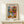 May include: Framed art poster featuring a colorful still life with flowers in a geometric blue and white vase, oranges with one cut in half, and background blocks of blue and coral pink. The poster displays "MATISSE" at top and "ART POSTER" at bottom. Shown in light wood frame on white shelf next to small white decorative object against cream wall.