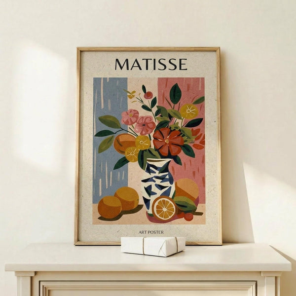 May include: Framed art poster featuring a colorful still life with flowers in a geometric blue and white vase, oranges with one cut in half, and background blocks of blue and coral pink. The poster displays "MATISSE" at top and "ART POSTER" at bottom. Shown in light wood frame on white shelf next to small white decorative object against cream wall.