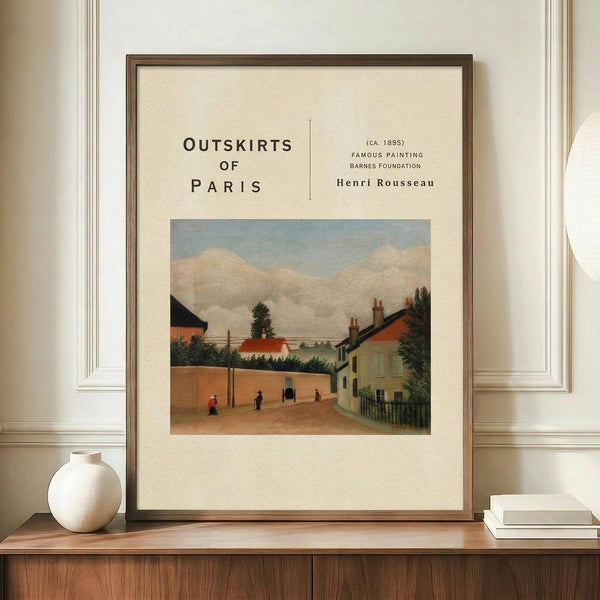 May include: Framed art print featuring Henri Rousseau's painting of a Parisian suburban street scene with houses, trees, and small figures under a cloudy sky. The cream-colored poster has vintage-style typography reading "Outskirts of Paris" and artist attribution. Displayed on wooden sideboard with white ceramic vase and books against cream paneled wall in modern interior setting.