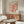 May include: Framed coral pink Matisse-inspired cut-out botanical poster displayed above a wooden sideboard in a modern living room. The artwork features organic leaf-like shapes in warm coral tones on cream background. Room shows white curved chair, glass oval coffee table, brass floor lamp, and small table lamp. Neutral walls and natural lighting create a mid-century modern aesthetic.