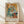 May include: Framed Pablo Picasso poster print leaning against white wall on light wood floor. Cubist artwork shows two abstracted figures in blue, orange, and cream tones sitting at a table. Natural light casts diagonal shadows across the scene. Light wood frame with cream matting surrounds the vintage-style art print.