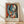 May include: Framed Pablo Picasso-style abstract portrait poster leaning against white textured wall on light wooden floor. Artwork features cubist woman with split blue and white face, black hair, red lips, geometric shapes in vibrant colors including orange, red, and yellow background. Natural light casts soft shadows across the scene. Light wood frame surrounds the vintage-style art print with cream matting and artist name below image.