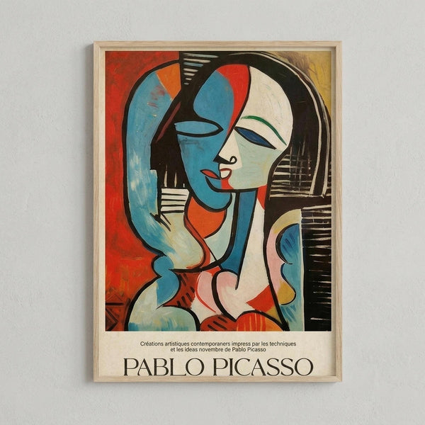 May include: Framed Picasso-style cubist artwork showing abstract woman's portrait in blue, red, orange and cream tones with geometric shapes and bold black lines, displayed in light wood frame against white wall