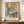 May include: Framed Picasso-style cubist artwork showing two women in soft blue, orange and cream tones, displayed on a wooden sideboard next to a small white ceramic vase and books. The poster features French text below the abstract figures and is set against cream-colored wainscoting in an elegant interior setting.
