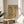 May include: Framed botanical poster with vintage-style typography reading "Nature's Essence" surrounded by stylized leaves, plants and geometric shapes in earthy green, rust, and blue tones on cream background. Wood frame sits on round wooden stool next to beige upholstered chair and potted plant in sunlit room with white walls.