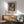 May include: Framed Picasso-style abstract portrait poster in cubist style featuring a woman's face in blue, red, and orange tones, displayed above a mid-century modern wood credenza with white ceramic lamp, next to a mint green upholstered armchair with wooden frame in a minimalist room with white walls and natural sunlight streaming across the scene.