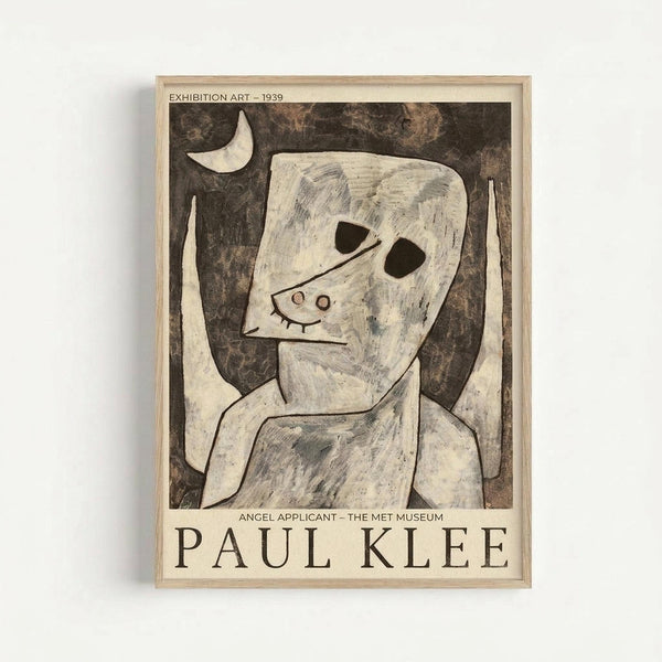 A framed exhibition poster featuring Paul Klee's abstract artwork "Angel Applicant" from 1939. The artwork shows a simplified, childlike figure with a white mask-like face, black oval eyes, and small curved mouth, set against a dark mottled background. A crescent moon appears in the upper left corner. The figure has geometric, elongated limbs rendered in pale tones with sketchy blue accents. Text at top reads "EXHIBITION ART - 1939" and bottom shows "ANGEL APPLICANT - THE MET MU