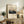 May include: Framed vintage-style poster showing Mount Fuji at sunset with pink sky and dark silhouetted landscape, displayed on rustic wooden sideboard alongside fern plant, books, ceramic vase and table lamp in warm-toned living room setting