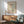 May include: Framed Matisse-style poster with colorful abstract cut-out shapes in coral, mint green, and cream tones, displayed above a mid-century modern wooden sideboard. Scene features a sage green upholstered armchair with wooden frame, white ceramic table lamp, and warm natural lighting creating soft shadows on white walls.