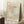 May include: Framed Matisse-style art print with pastel pink, mint green, and cream abstract cut-out shapes and cross-hatched patterns, leaning against white wall corner. Wooden frame, positioned next to small wooden side table with white coffee cup and saucer, on textured cream rug with beige throw blanket visible.