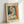 May include: Framed art print in light wood frame leaning against white wall, featuring abstract portrait of woman's face and torso in cubist style with geometric shapes in green, orange, yellow and cream tones. Text reads "PICASSO" at top with French description below the artwork.