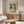 May include: Cubist-style portrait poster featuring a stylized woman with geometric facial features in green, orange, yellow and blue tones, displayed in thin wooden frame above mid-century walnut credenza with sliding doors. Modern living room setting with curved white chair, round glass coffee table, and warm natural lighting creating shadows on white walls.