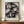 May include: Abstract geometric artwork in muted tones of gray, beige, and soft pastels featuring overlapping angular shapes, circles, and crystalline forms. The framed poster displays on a wooden sideboard next to a small white ceramic vase and stacked books against cream-colored paneled walls. The composition shows fragmented, cubist-style elements with layered translucent effects creating depth and movement throughout the piece.
