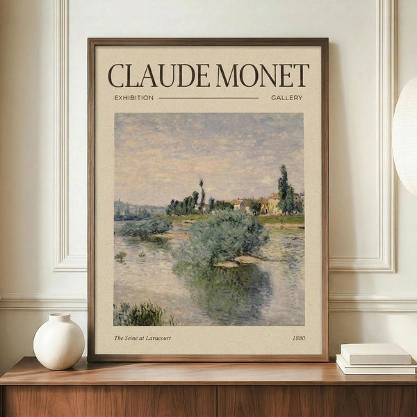 May include: Framed exhibition poster featuring Claude Monet's impressionist river landscape with soft blues, greens, and peachy tones, displayed on a wooden sideboard beside a cream ceramic vase and white books against beige wainscoted walls.