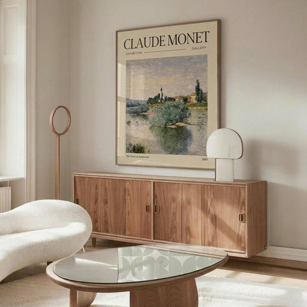 May include: Framed Claude Monet exhibition poster displayed above wooden sideboard in minimalist living room. The vintage-style poster features an impressionist river landscape with soft blues, greens and earth tones. Modern furniture includes cream sculptural chair, glass oval coffee table, and sleek table lamp. Neutral walls and natural lighting create serene gallery-like atmosphere.