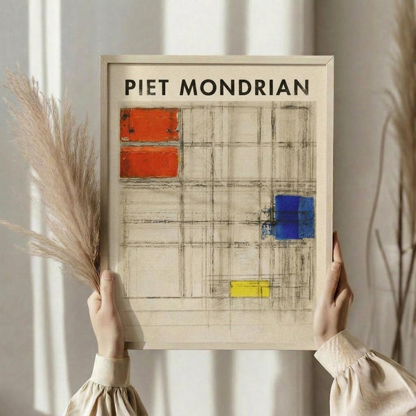 May include: Person in cream ruffled sleeve top holding framed Mondrian-style art print with geometric grid pattern featuring red, blue, and yellow rectangular blocks on beige background. Natural dried wheat stems visible alongside. Soft neutral lighting and white curtains in background create minimalist aesthetic.