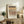 May include: Framed art print with abstract geometric patterns in earth tones - browns, tans, and cream with black accents arranged in horizontal bands. The poster displays in a light wood frame on a rustic wooden sideboard alongside a fern plant, ceramic vase, and books in a warm, naturally-lit room setting.