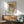 May include: Framed Picasso-style cubist portrait poster hanging on white wall above wooden sideboard, featuring abstract female figure in blues, greens, oranges and yellows. Scene shows mid-century modern furniture including mint green upholstered armchair with wooden frame, round coffee table, and white ceramic table lamp. Natural sunlight creates dramatic shadows across the minimalist room setting.