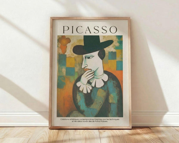 May include: Framed poster print in light wood frame leaning against white wall on wooden floor. Features cubist-style portrait of figure in dark green hat and clothing with white ruffled collar, hand near face in contemplative pose. Geometric background with blue, orange, and yellow squares. Text reads "PICASSO" at top with French description below artwork.