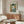 May include: Framed Picasso-style portrait poster showing figure in hat and ruffled collar against colorful checkered background, displayed above mid-century walnut credenza in modern living room with white sculptural chair, glass coffee table, and cream table lamp