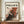 May include: Framed abstract art poster with Jackson Pollock-inspired splatter painting in black, red, and white colors. Bold "POLLOCK" text at top with "CHAOS AND CREATIVITY 1912-1956" subtitle. Wooden frame displayed on walnut credenza beside white ceramic vase and stacked books against cream walls with white trim molding.