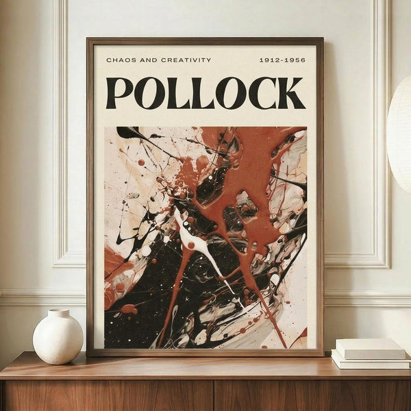 May include: Framed abstract art poster with Jackson Pollock-inspired splatter painting in black, red, and white colors. Bold "POLLOCK" text at top with "CHAOS AND CREATIVITY 1912-1956" subtitle. Wooden frame displayed on walnut credenza beside white ceramic vase and stacked books against cream walls with white trim molding.