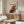 May include: Jackson Pollock abstract art poster with red, black and white paint splatters hanging above a wooden sideboard in a modern living room. White curved chair and glass coffee table visible in foreground. Poster shows chaotic drip painting style with dynamic brushstrokes and paint drips against cream background.