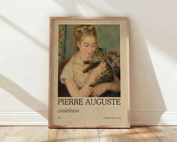 May include: Framed exhibition poster featuring Renoir's 1875 painting of a blonde woman in white dress holding a tabby cat, displayed against white wall on light wooden floor. Poster has cream background with brown text reading "PIERRE AUGUSTE exhibition" and "Woman with a Cat". Natural window light creates soft shadows across the scene.