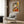 May include: Framed Picasso-style cubist poster featuring geometric woman in orange, yellow, and gray tones, displayed above beige armchair with patterned pillow in modern room with wood paneling, brass floor lamp, and dark side table with open book.