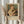 May include: Hands holding a framed vintage art print featuring a blonde woman in cream clothing embracing a tabby cat, with "PIERRE AUGUSTE exhibition" and "1875 Woman with a Cat" text below the image. Neutral beige frame against white curtained window with dried wheat stems visible on left side.
