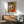 May include: Framed Picasso-style cubist art print featuring a seated woman in geometric orange, yellow, and gray tones, displayed above a mid-century modern wooden credenza with white ceramic lamp. Mint green upholstered armchair with walnut frame sits nearby in bright, minimalist living room with white walls and natural lighting.