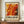 May include: Framed exhibition poster featuring abstract artwork with flowing orange, red, and yellow paint splatters reminiscent of Jackson Pollock's style. The poster advertises a fictional 2030 exhibition titled "Embrace the Chaotic Realm of Creativity" by Abstract Visionary. Displayed on wooden sideboard next to white ceramic vase and stacked books against beige wall with white trim molding.