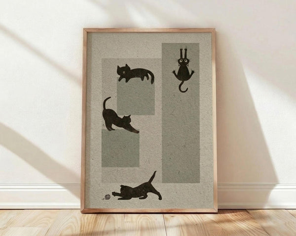 May include: Framed poster with playful black cat silhouettes on cream textured paper background, displayed in light wood frame leaning against white wall on wooden floor with natural sunlight shadows. Features four whimsical cats in different poses - sleeping, stretching, hanging upside down, and playing with a ball.